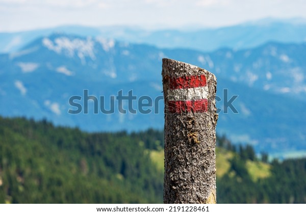 Close-up of a red and white trail sign\
(trail marker) painted on a pine tree trunk, with blurred mountain\
landscape in the background. Alps, Austria,\
Europe.