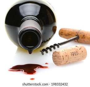 Closeup of a red wine bottle with a drip and wine spill in the foreground. A cork screw and cork to one side on a white background with slight reflection. Shallow depth of field with focus on the drip