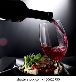 Closeup Of Red Wine Pouring Into Glass With Meat And Cheese