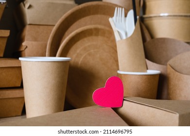 Close-up Of A Red Wooden Heart On A Pile Of Cardboard Kitchen Items. The Concept Of Protection And Care For The Environment.