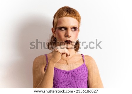 Close-up of a red-haired non-binary person posing on a white background in a purple dress. The man has a doubtful, uncertain, thoughtful expression. Concept of people does not identify with any gender