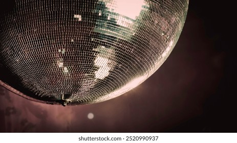 Close-up of a reflective mirror disco ball hanging from the ceiling spinning in dim lighting with scattered light bokeh, capturing a vintage retro luxury party celebration background. - Powered by Shutterstock