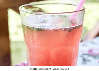 Close-up of a refreshing cold raspberry lemonade drink served in a tall glass with ice cubes, fresh mint leaves, and a pink straw.
