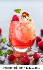 Close-up of a a refreshing red translucent drink with ice and raspberries. The juice is garnished with a green leaf, and therer are pieces of ice and rapsberries scattered around the drink.
