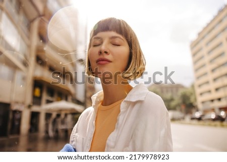 Close-up of relaxed young caucasian woman closing her eyes enjoying walk during day. Brown-haired with bob haircut wears white clothes. Happy weekend concept. Stock photo © 