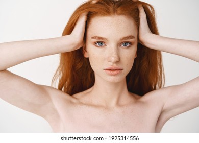 Close-up Of Relaxed Young Redhead Woman With Pale Skin And Freckles, Massaging Natural Red Hair, Standing Naked Without Make-up On White Background.