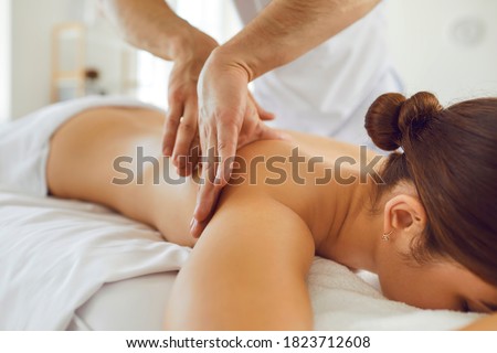 Closeup of relaxed young woman lying face down on massage table enjoying delicate body massage done by professional masseur in modern wellness center or luxury spa salon.