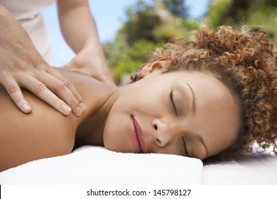Closeup of relaxed young woman receiving shoulder massage from masseuse at spa