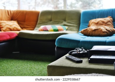 Close-up of remote control, game console and disc packaging on table in living room. Horizontal photo