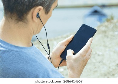 Close-up of remote worker using smartphone with earbuds. Symbolizes location-independent career, outdoor office concept, work-travel balance, flexible employment freedom, virtual meeting participation