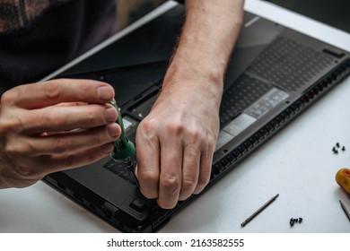 close-up of the repairman's hands unscrewing the screws from the laptop case with a screwdriver for its repair and maintenance. repair and maintenance of laptops. selective focus.