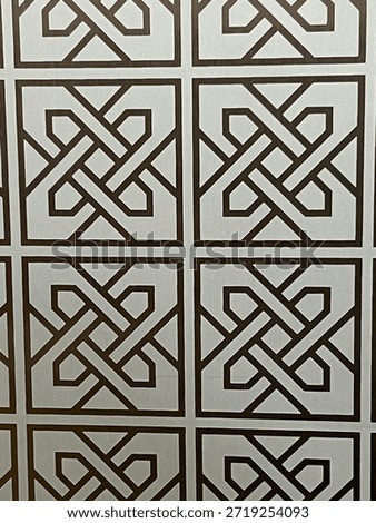 Close-up of a repeating geometric pattern featuring interlocking angular shapes in dark brown lines on a light gray background, forming a tiled lattice design.