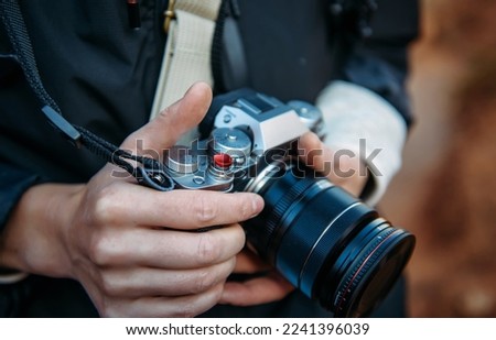 Close-up of reporter's hands holding digital camera. Adult woman's fingers touches photo camera, selective focus, blurred background.