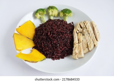 Close-up Of Riceberry Cooked And Chicken Breast With Boiled Broccoli And Pumpkin On A White Plate On A White Background Healthy, Clean Organic Food, Rich In Antioxidants And High In Fiber