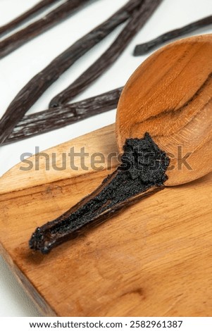 Close-up of rich vanilla bean paste in a wooden spoon, surrounded by aromatic dried vanilla pods on a cutting board