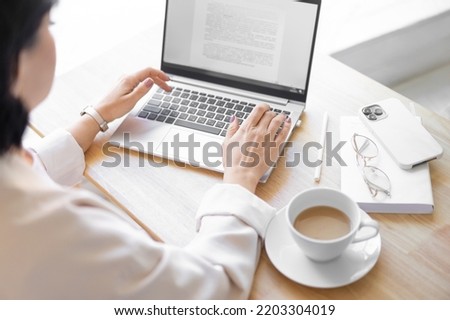 Close-up of the right hand. Unrecognizable brunette typing on a laptop keyboard. Sitting at a wooden table, drinking coffee. Selective focus. Blurred foreground.