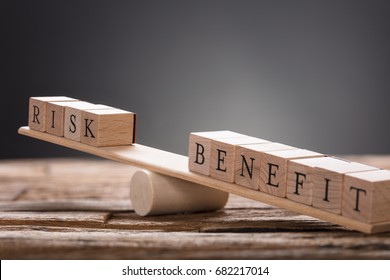 Closeup Of Risk And Benefit Wooden Blocks On Seesaw Against Gray Background