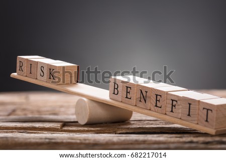 Closeup of risk and benefit wooden blocks on seesaw against gray background
