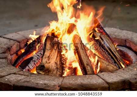 Close-up, roaring fire with blurred flames from wood logs in a stone firepit