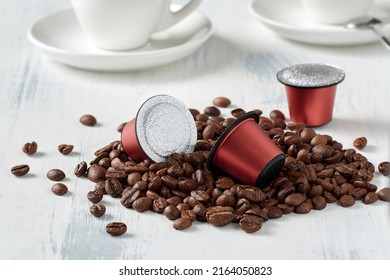 Closeup of roasted coffee beans and coffee capsules for a capsule coffee machine. On a light background with espresso cups.