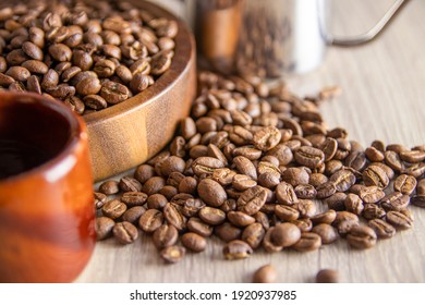 A close-up of roasted coffee beans spilled around a wooden bowl and a cup, showcasing their rich textures and colors on a light wooden surface. - Powered by Shutterstock