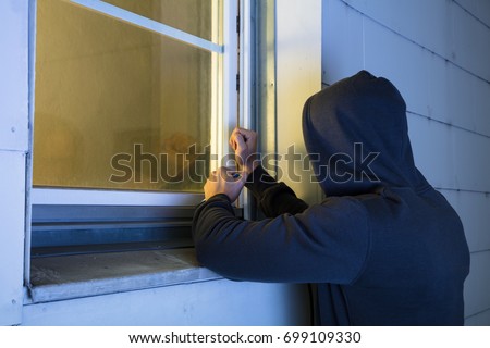 Close-up Of Robber In Hood Using The Red Crowbar To Open The Glass Window