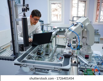 Close-up robot arm. Engineer is working on laptop to programming smart factory automation and automated car on production line. Industry 4.0 concept; artificial intelligence in smart factory.