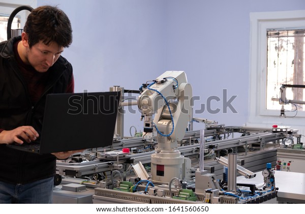 Close-up of Robot arm. Engineer is working on\
laptop to programming robot arm and automated car on production\
line is waiting. Industry 4.0 concept; artificial intelligence in\
smart factory.