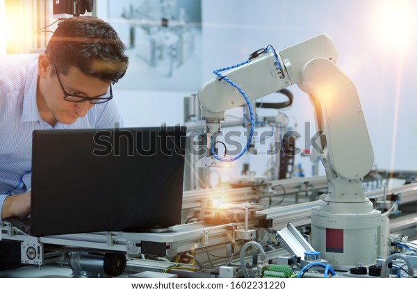 Close-up robotic arm. Engineer is working on\
laptop to programming smart factory automation and automated car on\
production line. Industry 4.0 concept; artificial intelligence in\
smart factory.