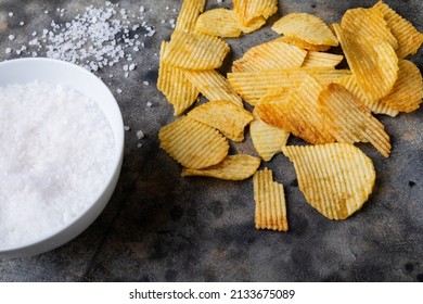 Close-up Of Rock Salt In Bowl With Potato Chips On Table. Unaltered, Unhealthy Food, Snack, Seasoning And Salty Snack.