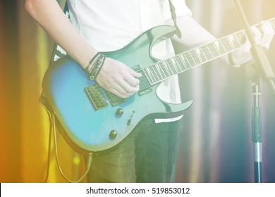 Closeup Rockstar On Stage Playing On Electro Guitar. Male Guitarist In A White Shirt.