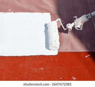 Closeup of the roller applying a layer of white rubber waterproofing paint to the floor of the building's roof. Waterproof and moisture-sealing paint. Heat treatment due to climate change.