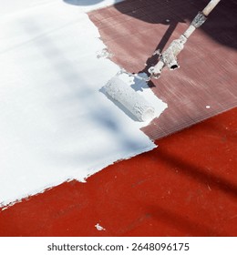 Closeup of a roller applying a layer of white rubber waterproofing paint with reinforcing fiberglass mesh to the building terrace. Waterproof and sealant paint. Heat treatment due to climate change.
