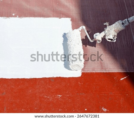 Closeup of the roller applying a layer of white rubber waterproofing paint to the floor of the building's roof. Waterproof and moisture-sealing paint. Heat treatment due to climate change.
