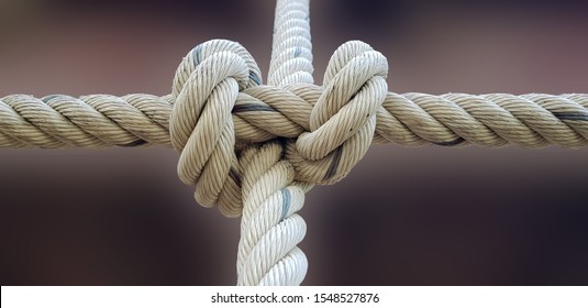 Close-up of rope knot line tied together with bridge background. White rope tied in a knot for adventure.Rope, tie a knot tied to a mesh of metal poles for children to climb.