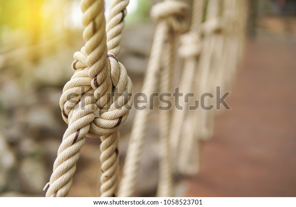 Close-up of rope knot\
line tied together with bridge background. White rope tied in a\
knot for adventure.Rope, tie a knot tied to a mesh of metal poles\
for children to climb.\
