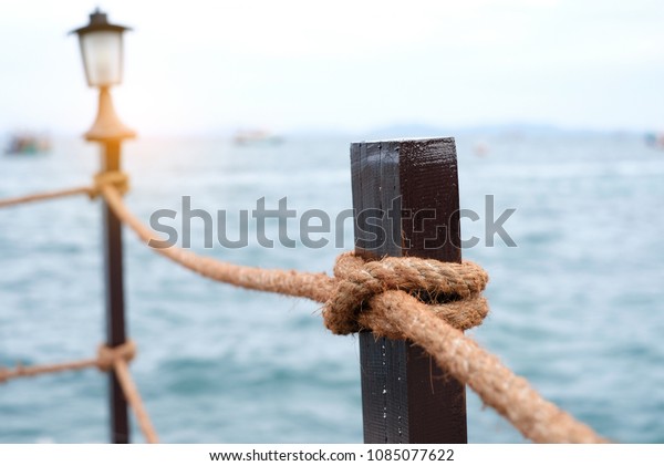 Close-up of\
rope knot line tied together with bridge in the sea background.\
White rope tied in a knot for adventure.Rope, tie a knot tied to a\
mesh of metal poles for children to\
climb.