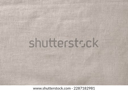 Closeup of rough, crumpled burlap texture made of flaxen textile material. Vintage grunge background with soft beige tones