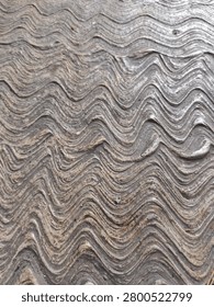 Close-up of rough grey cement surface with undulating curved ridge patterns.