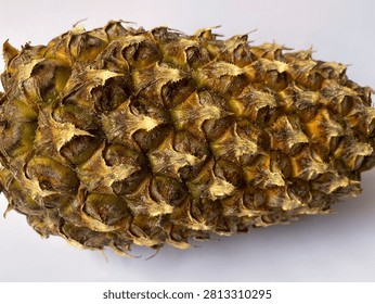 A close-up of a pineapple’s rough outer skin, featuring brown, golden, and green tones with sharp, spiky textures against a plain background.