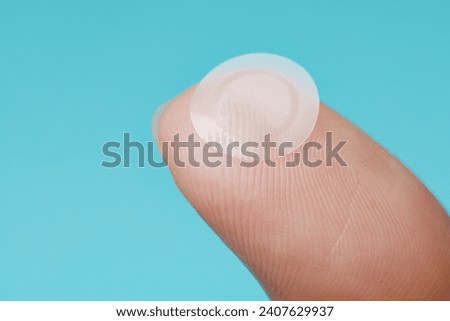 Close-up round acne patch on finger on blue background. Acne patches for treatment of pimple and rosacea close-up. Facial rejuvenation cleansing cosmetology