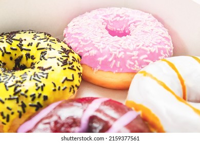 Closeup round colored donuts with sprinkles and topping. Glazed doughnut box. Pastel pink background. Donuts with different flavors - caramel, chocolate, gum.