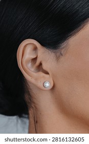Close-up of round silver stud earring with sparkling gemstone worn on female ear against soft neutral background