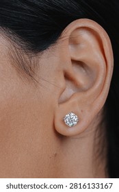 Close-up of round silver stud earring with sparkling gemstone worn on female ear against soft neutral background