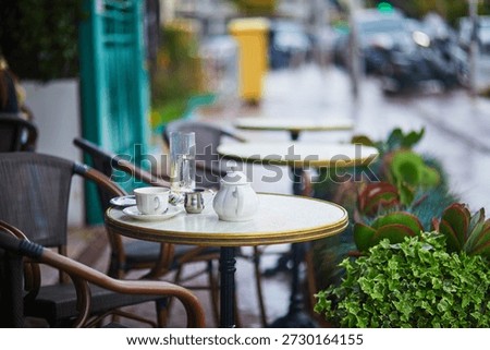 Close-up of a round table set with white porcelain teapot, cup, and glass of water at a quiet Parisian-style outdoor cafe.