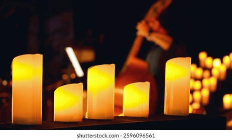 Primer plano de una fila de velas encendidas en primer plano con un fondo borroso de un contrabajista. Concierto de velas