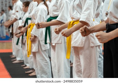 A close-up of a row of young athletes in white karate kimonos with clenched fists. A photo for a demonstration or karate competition. Energy and concentration concept.