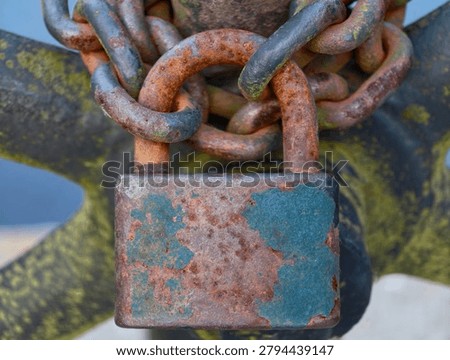Close-up of a rusted padlock and tangled chains on a weathered metal surface. The image shows rough textures, fading blue-green patina, and sunlight