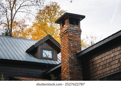 Close-up of a rustic cabin's brick chimney and wooden siding, framed by autumn-colored trees, capturing the essence of rural living and natural beauty. - Powered by Shutterstock