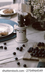 Close-up of a rustic dining table with blueberries, cutting board, and vintage kerosene lamp.